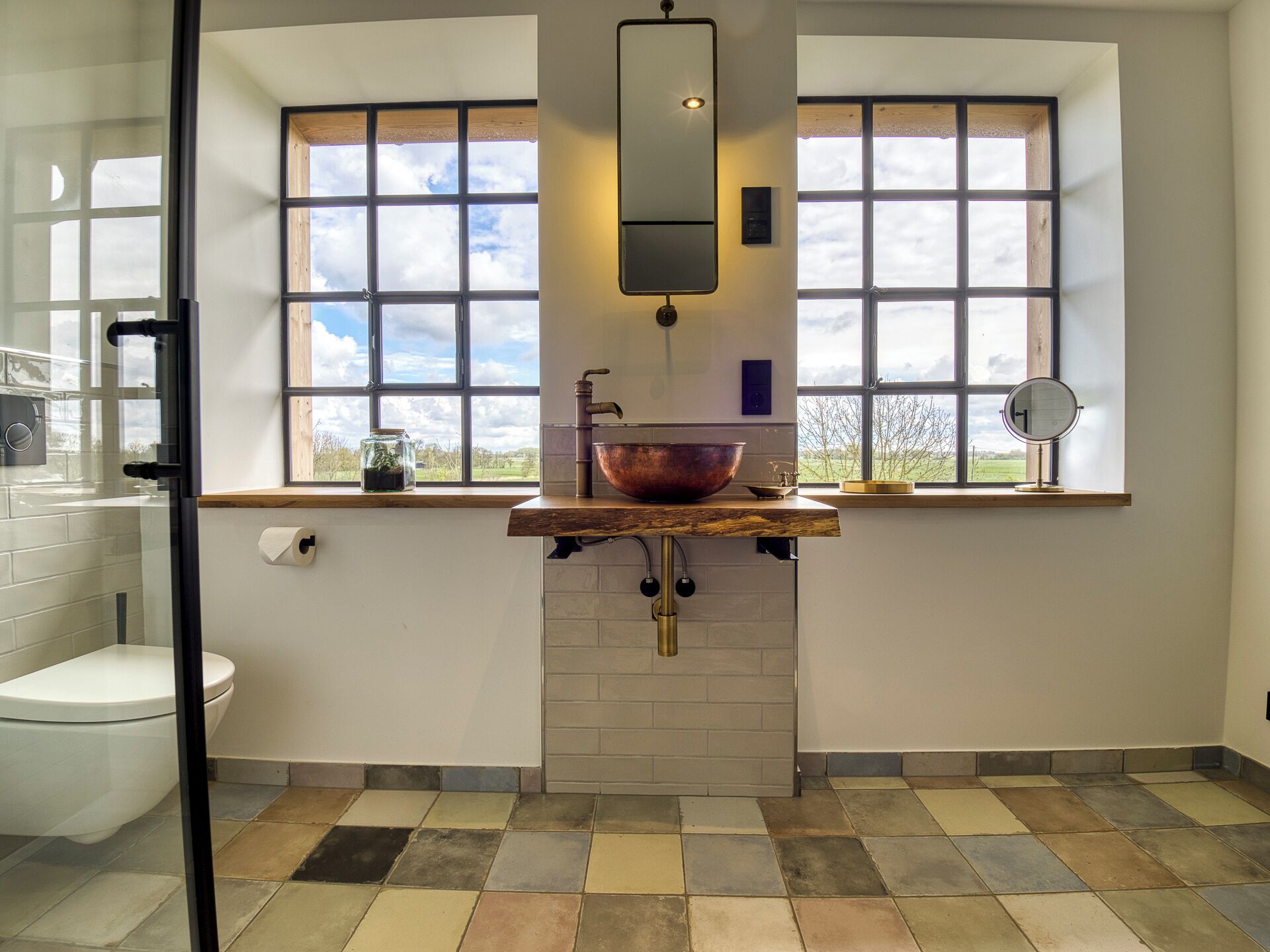Ein Badezimmer mit großem Fenster, einem Kupferbecken, einem Spiegel und einer Toilette.