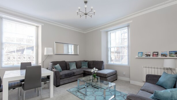 A modern living room with a sectional sofa, a glass coffee table, and a dining area with a white table and chairs. - Grassmarket Modern Two Bedroom Flat  (Edinburgh)