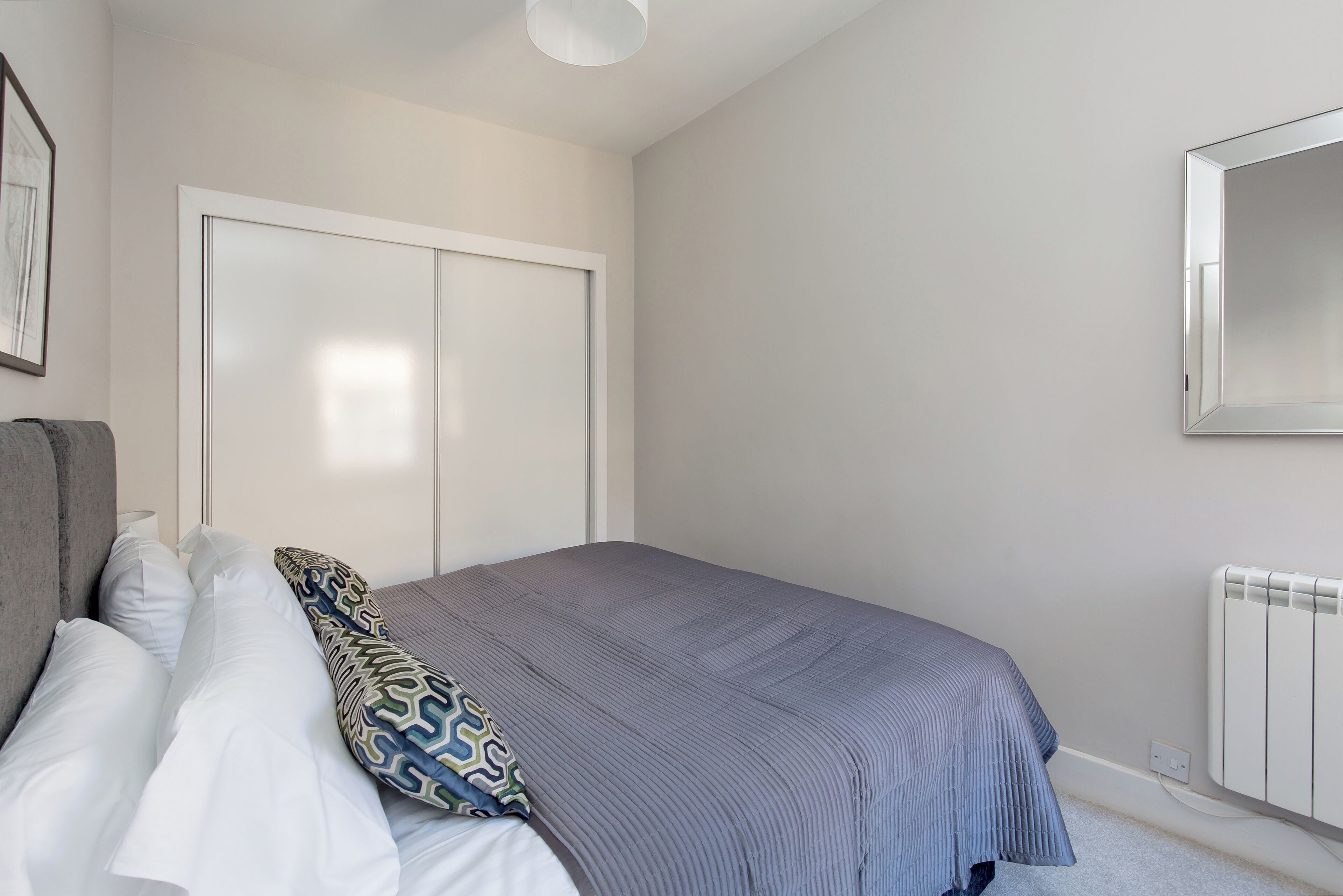 Une chambre à coucher avec un lit, une armoire, un radiateur et un miroir au mur.