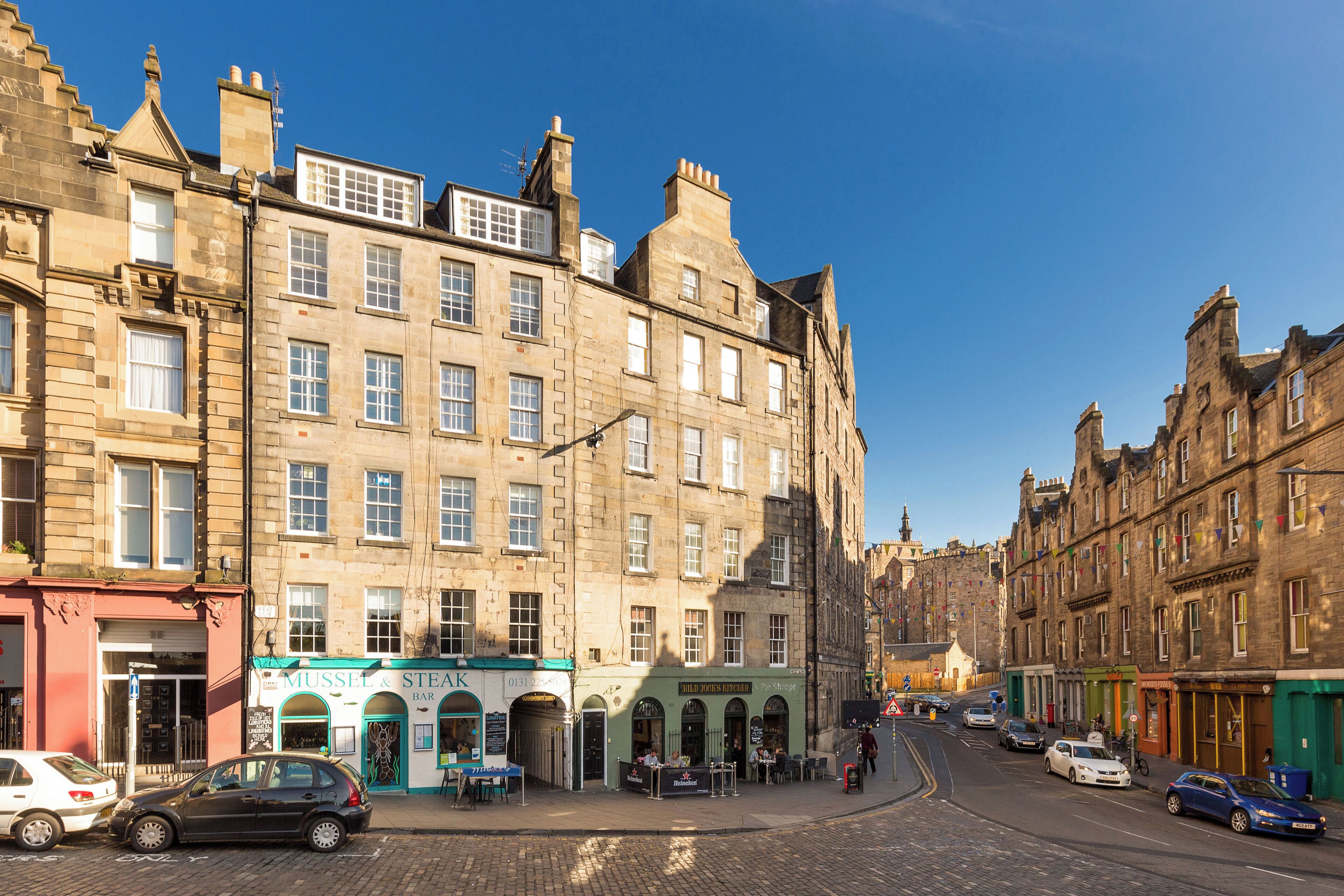 A street view with historic buildings, a café, and parked cars.