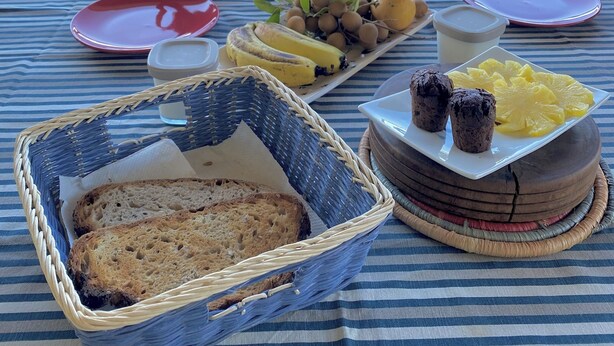 A picnic setup with a table set for two, featuring plates, cups, a basket of bread, and a plate of fruits. - The plaid zebra (Entre-Deux)
