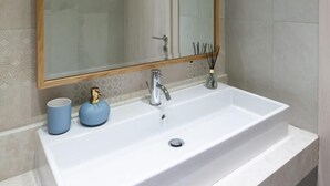 Un baño con lavamanos blanco, un espejo grande y un perchero para toallas.