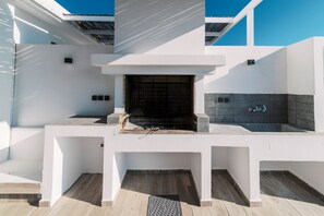 A modern outdoor kitchen with a built-in grill, a sink, and a tiled backsplash. - Villa Nissos in Lindos (Theotokos)
