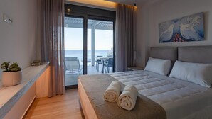 Habitación de hotel con cama, vista al mar, zona de comedor y un cuadro en la pared.