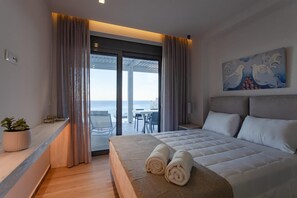 A hotel room with a bed, a view of the sea, a dining area, and a painting on the wall. - Villa Nissos in Lindos (Theotokos)