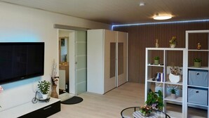 A modern living room with a flat-screen TV, a bookshelf, and a dining area with a round table. - New modern vacation apartment by the forest. (Bückeburg)