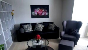 A modern living room with a black sofa, a black armchair, a glass coffee table with a red flower, and a floral painting on the wall. - New modern vacation apartment by the forest. (Bückeburg)