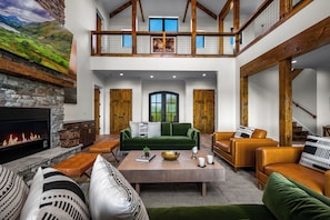 Uma sala de estar ampla com lareira de pedra, um sofá verde e escada de madeira.
