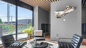 Eine moderne Lobby mit zwei Ledersesseln, einem Glastisch, einem Blumentopf und einem großen abstrakten Kunstwerk an der Wand.