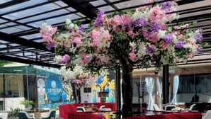 Un comedor interior con asientos tapizados en rojo, un gran árbol con flores y un techo de vidrio.