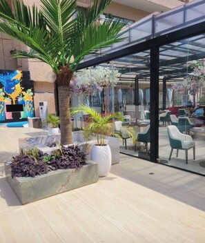 Un espace extérieur aménag é avec des palmiers, des jardinières et une partie fermée par des parois de verre, comprenant des chaises et des tables.
