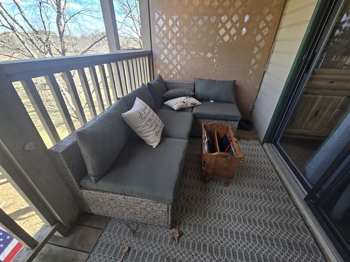 Un espace extérieur aménagé, abrité et doté d’un canapé, de coussins et d’une petite table en bois.