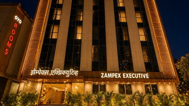 En byggnad med skylten ”ZAMPX EXECUTIVE”, stora fönster och en väl upplyst entré med krukväxter.