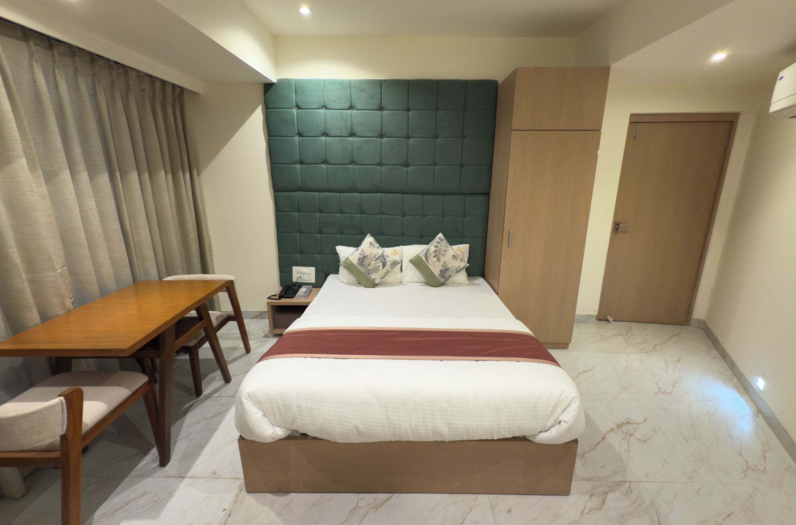 A hotel room with a bed, a wooden desk, a chair, a nightstand, and a wardrobe.