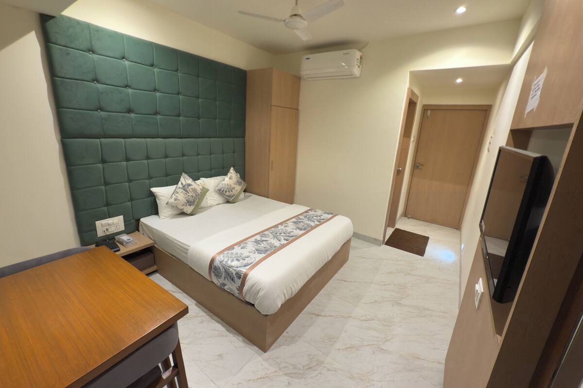 Une chambre d’hôtel équipée d’un lit, d’un bureau en bois, d’un ventilateur de plafond, d’un climatiseur et d’une télévision.
