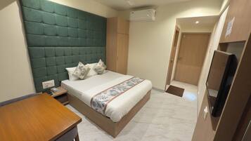 Habitación de hotel con cama, escritorio de madera, ventilador de techo, equipo de aire acondicionado y televisor.