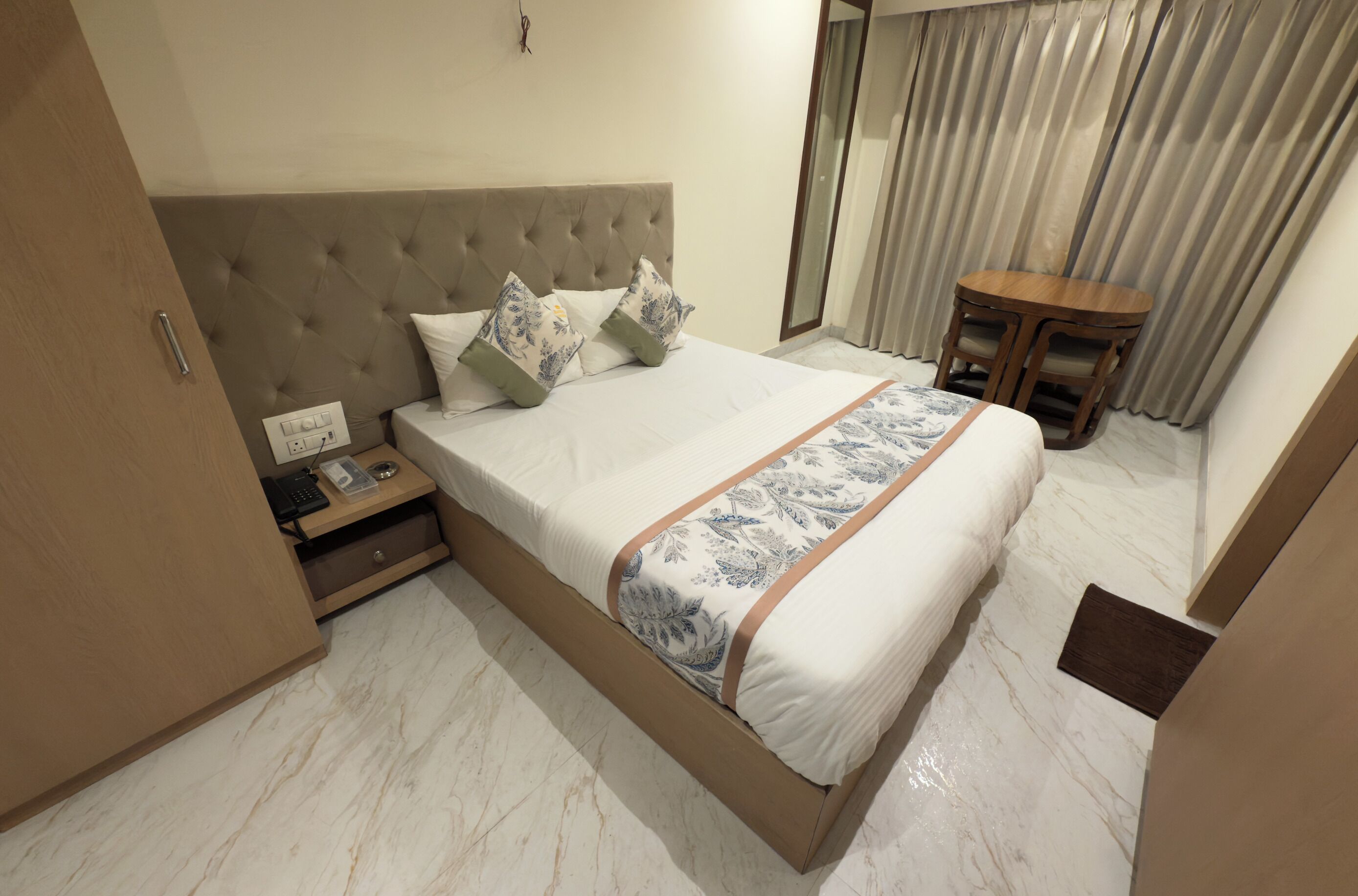 Una camera d'albergo ordinata con un letto grande, un comodino, un tavolino in legno e uno specchio.