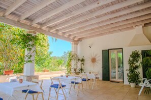 An outdoor patio with white tables and chairs, surrounded by potted plants and a wooden ceiling. - Casa Giada nel cuore del Salento (Gallipoli)