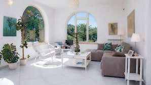 A modern living room with a white sofa, a white coffee table, and a white armchair. There are potted plants and a television on a stand. - Casa Giada nel cuore del Salento (Gallipoli)