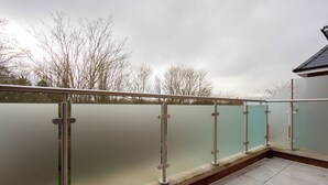 A balcony with a metal railing and a glass barrier, overlooking a building and trees. - Beautiful 4 Bed House - Close to Windsor Castle! (Windsor)