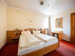A double bed with white linens, a wooden headboard, two bedside tables with lamps, a small bedside table with a mirror, and a red carpeted floor. - Geraumige Ferienwohnung im Sammareier Gutshof in Bad Birnbach (Bad Birnbach)