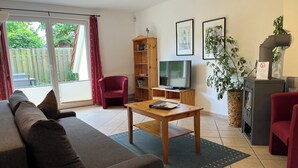 Una sala de estar con un sofá, una mesa de centro de madera, un televisor, una estantería y una planta en maceta.
