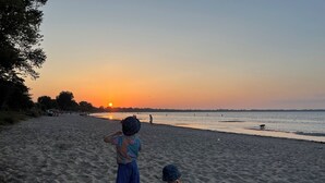 Escena de playa con dos niños jugando en la arena, un atardecer de fondo y un mar tranquilo.