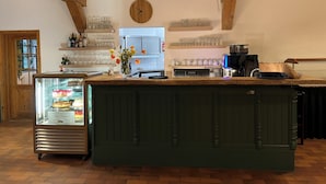 Una cocina con vigas de madera, un reloj, una cafetera y una vitrina con pasteles.