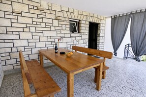 Ein Holztisch mit Bänken, eine Steinmauer, ein kleines Fenster und Blick ins Freie.