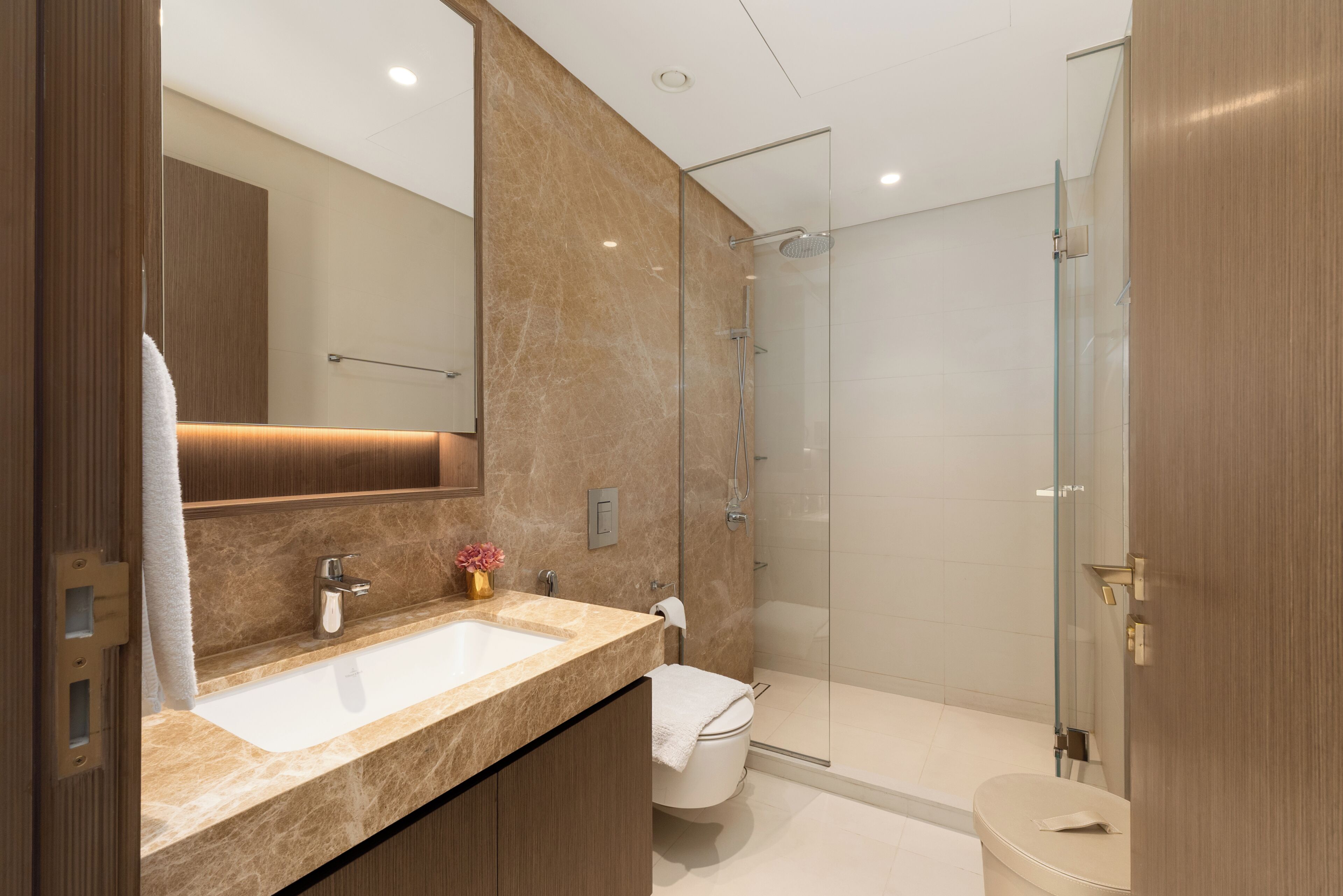 Een moderne badkamer met een dubbele wastafel, een douchecabine van glas en een houten wastafelmeubel.