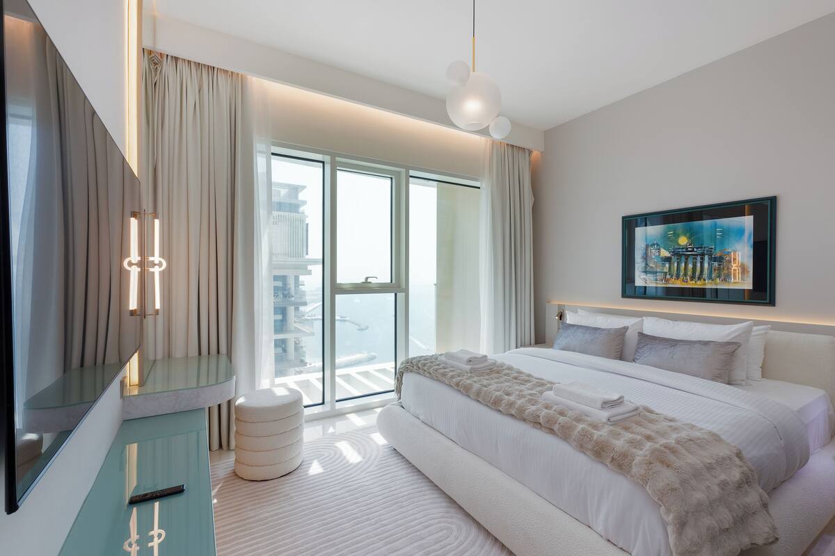 A modern hotel room with a large bed, a glass door leading to a balcony, and a painting on the wall.
