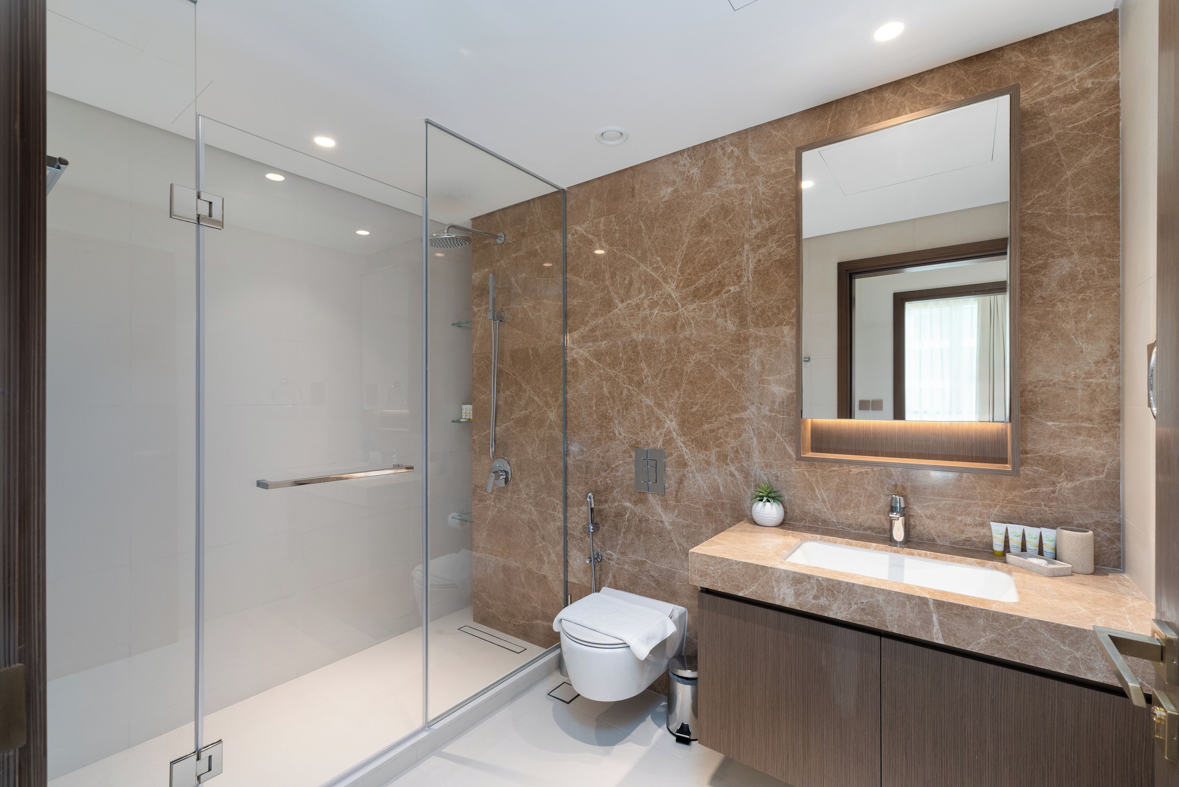 A modern bathroom with a glass shower enclosure, a marble vanity, and a large mirror.