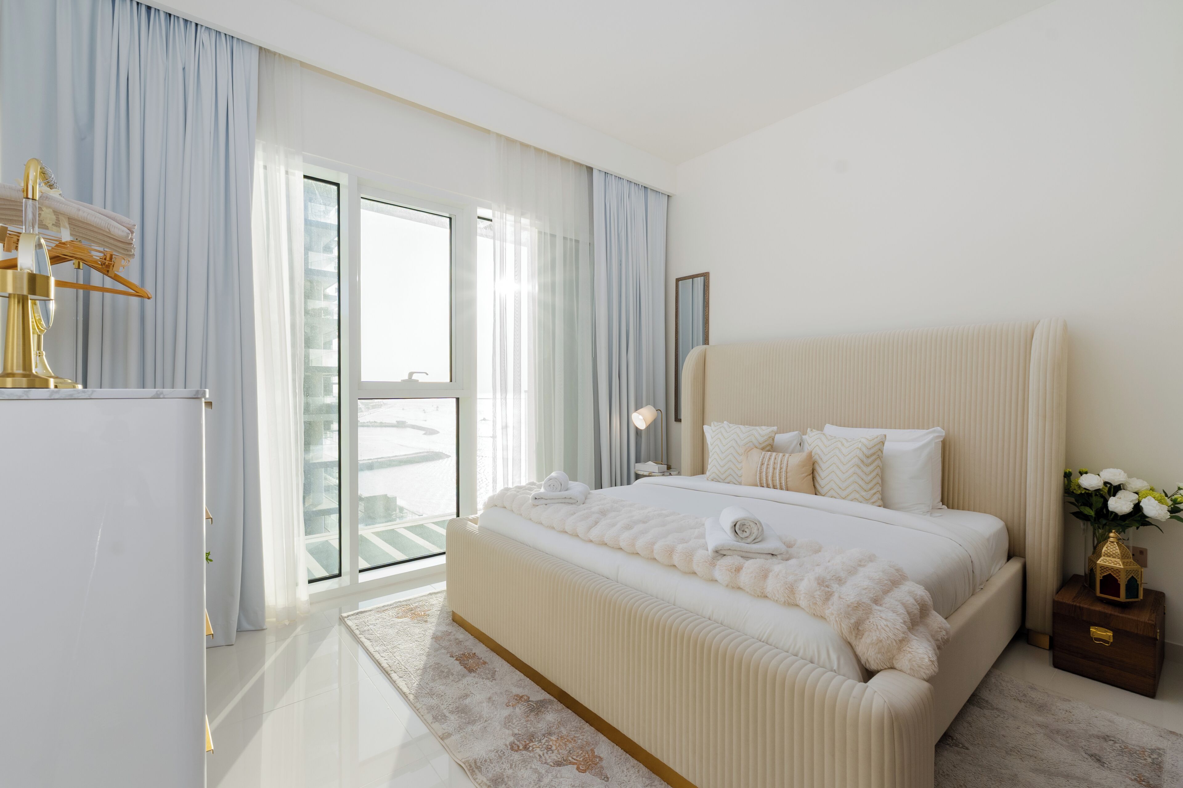 A modern bedroom with a large bed, a wardrobe, a nightstand, and a view of the outside.