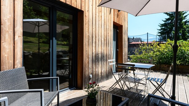 An outdoor patio with wooden flooring, a table, chairs, and a large umbrella.