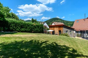 A residential area with a grassy lawn, wooden house, and a mountain in the background.