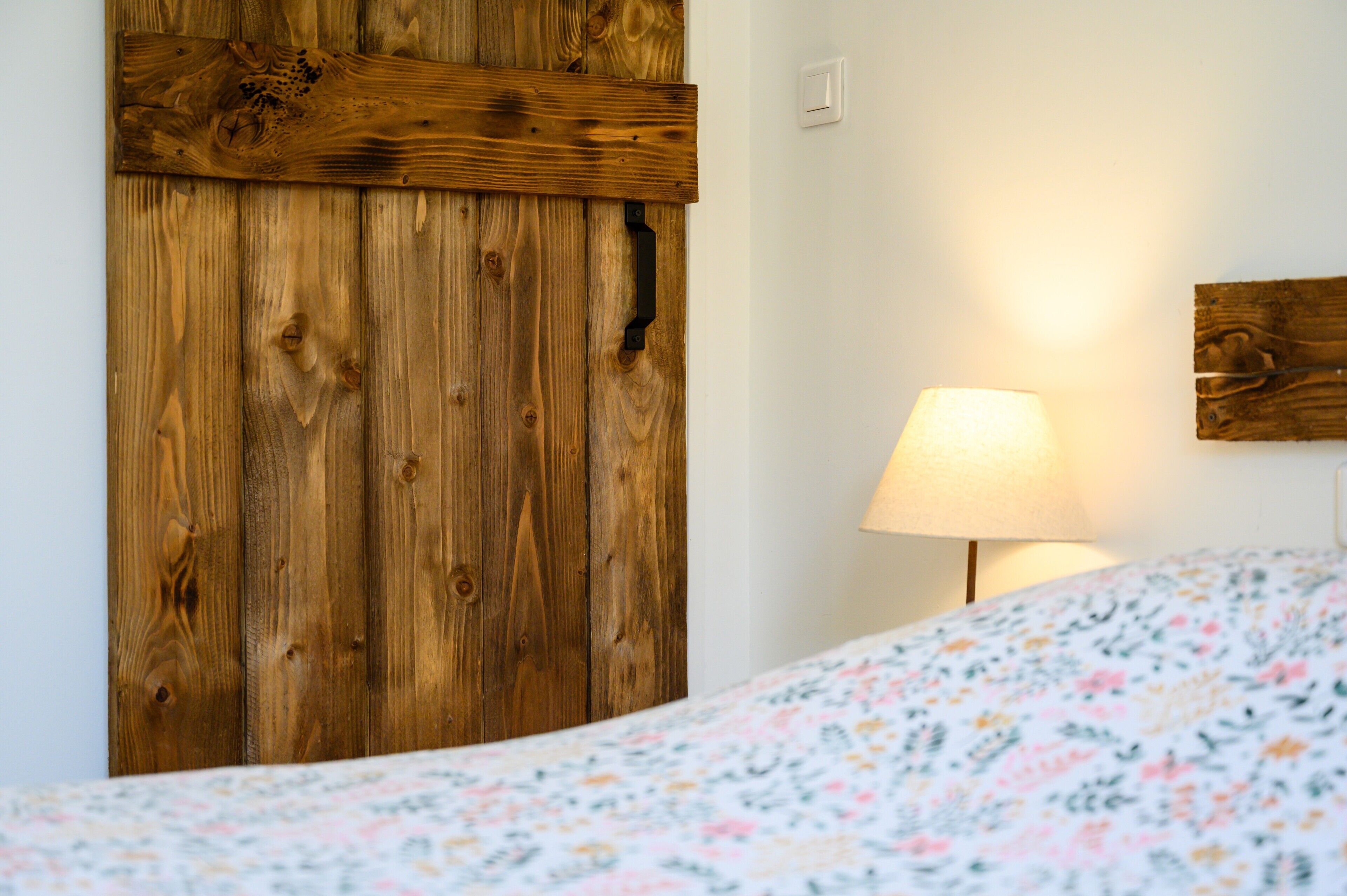 Une chambre avec une armoire en bois, un lit recouvert d’une couvre-lit à motifs floraux et une lampe de chevet.