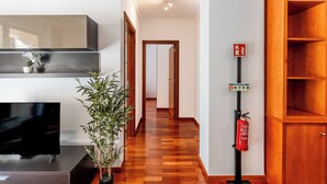 Un intérieur moderne avec un plancher en bois, un téléviseur à écran plat, une plante en pot et un extincteur fixé au mur.