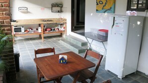 A small kitchenette with a microwave, sink, and a refrigerator. There is a wooden table with chairs and a small house model on it. - Bella vida274 (Porto Seguro)