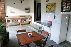 A small kitchenette with a microwave, sink, and a refrigerator. There is a wooden table with chairs and a small house model on it. - Bella vida274 (Porto Seguro)