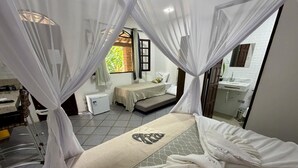 A bedroom with a bed, a small bedside table, a window with curtains, a bathroom with a sink and mirror, and a tiled floor. - Bella vida274 (Porto Seguro)