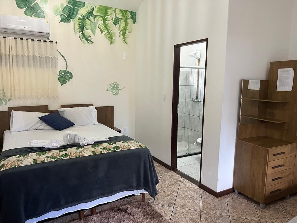 Un dormitorio con cama, cómoda de madera, baño con puerta de cristal y pared con diseño de hojas.
