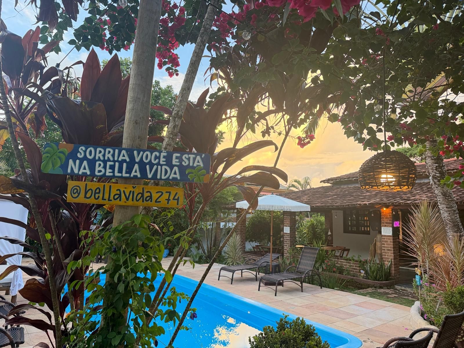 A pool area with lounge chairs, a sign with a message, and a house in the background.