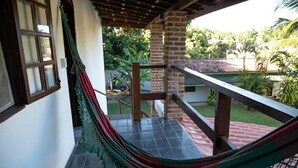 A hammock on a balcony with a view of a garden and a building in the background. - Bella vida274 (Porto Seguro)