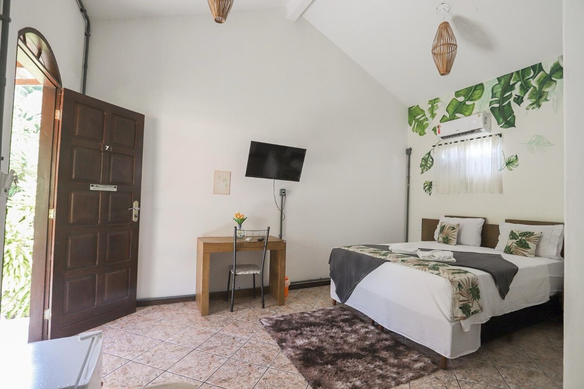 Un dormitorio con cama, escritorio, silla, televisor y ventana con cortinas.