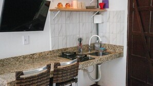 A compact kitchen with a granite countertop, a built-in stove, a sink, and a wall-mounted TV. - Bella vida274 (Porto Seguro)