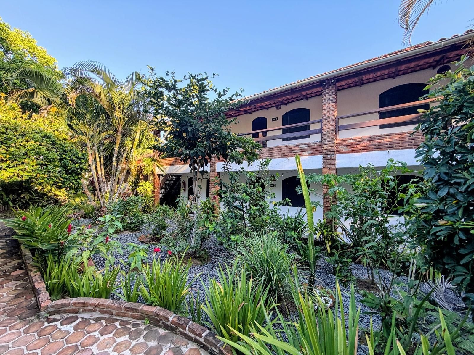 A building with a brick facade, multiple windows, and a garden with various plants and a stone pathway.