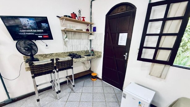 A compact kitchen with a gas stove, a fan, a refrigerator, and a TV mounted on the wall. - Bella vida274 (Porto Seguro)