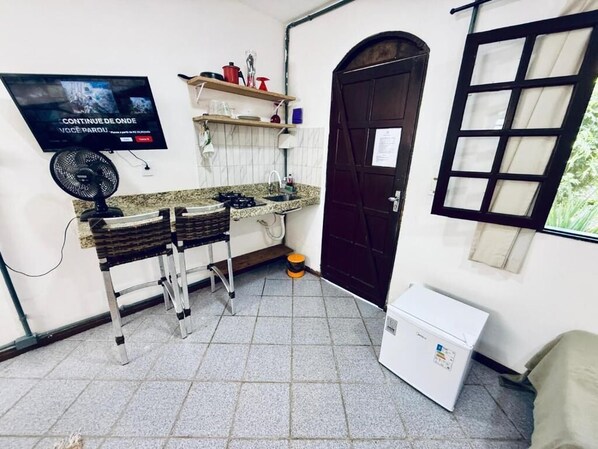A compact kitchen with a gas stove, a fan, a refrigerator, and a TV mounted on the wall. - Bella vida274 (Porto Seguro)