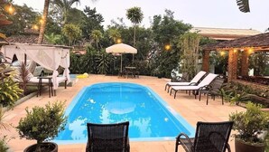 A swimming pool with lounge chairs and a covered seating area, surrounded by potted plants and palm trees. - Bella vida274 (Porto Seguro)