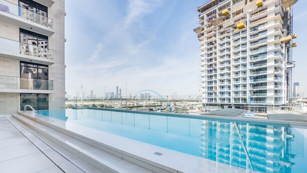 A modern building with a rooftop pool, a view of the city skyline, and a construction site in the background. - Tranquil Studio with City View, O10 Building (Dubai)